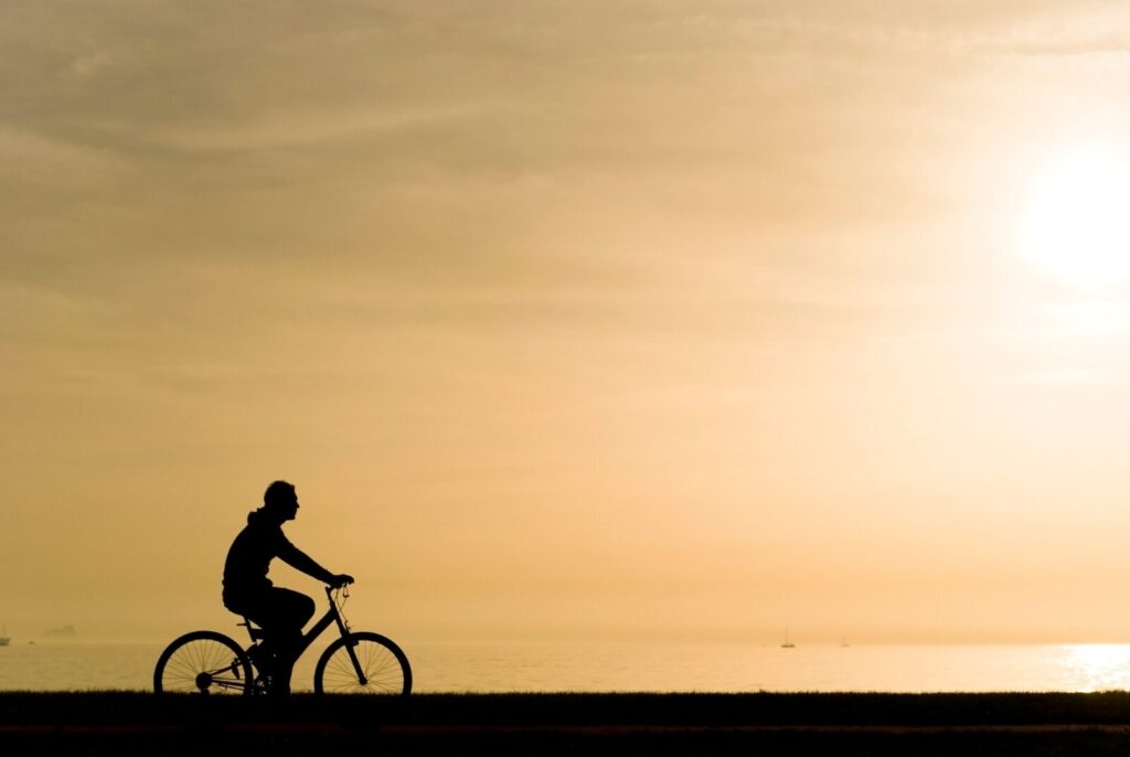 a silhouette of a man on a bicycle, calm evening sea in the background
