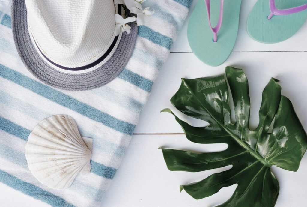 Summer beach flat lay with hat, towel, flip flops, and shells for no-spend activities inspiration