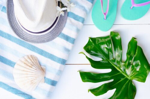 Summer beach flat lay with hat, towel, flip flops, and shells for no-spend vacation inspiration