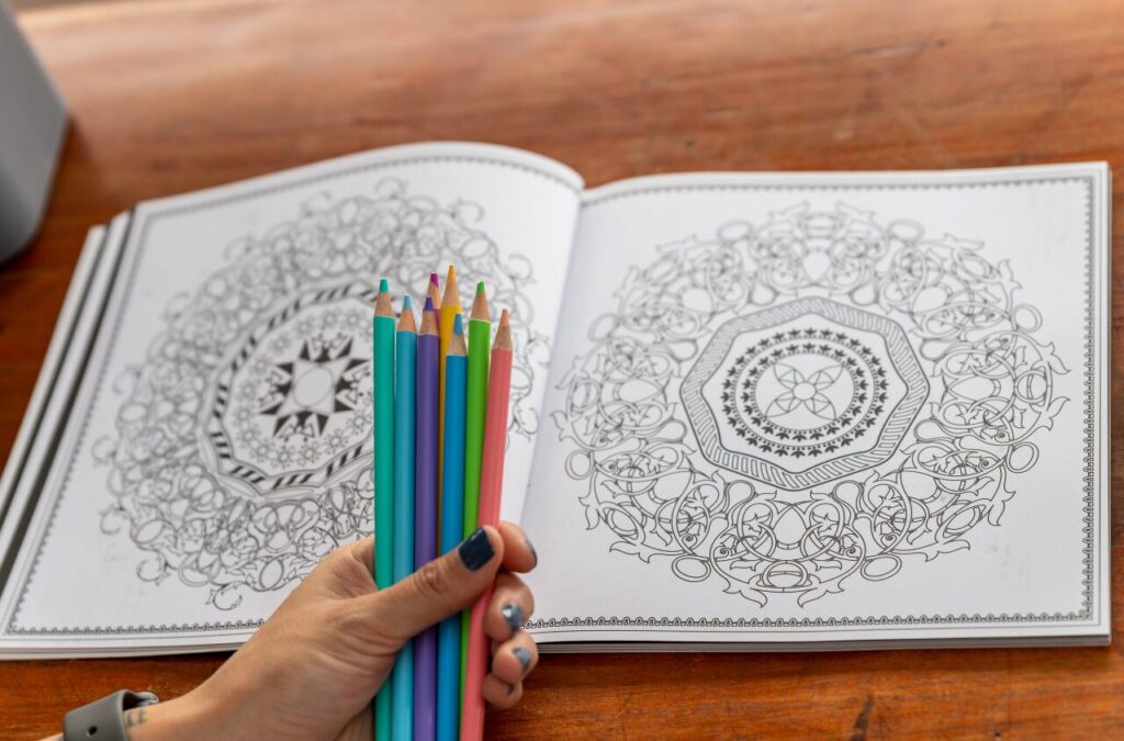 adult coloring hand holding colorful pencils in front of coloring book - example of cheap hobbies idea